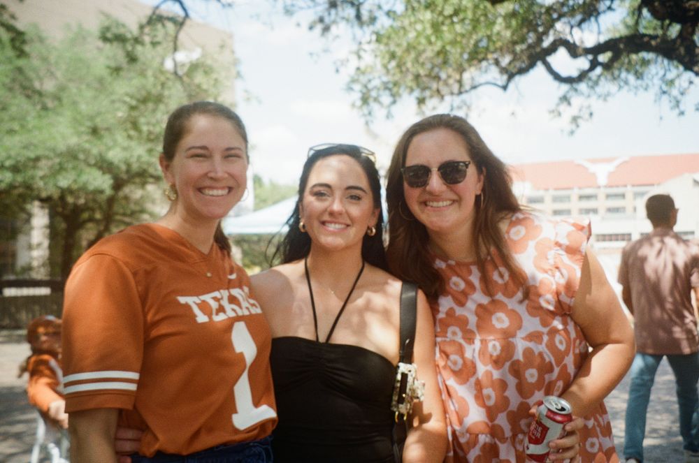 Three adult guests standing together at the Longhorn Strokes tailgate before a home football game.